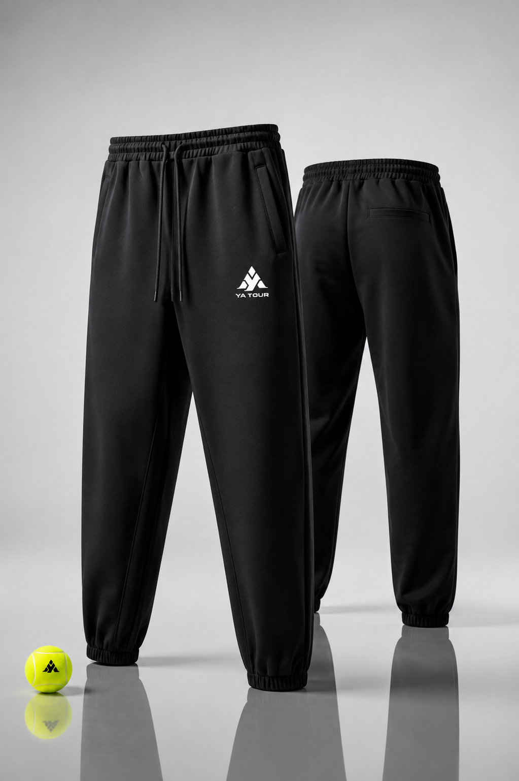 YA TOUR Unisex Heavyweight Fleece Joggers – Black, front and back editorial view showing mid-rise elastic waistband with drawstring, YA TOUR logo, side pockets and tapered ankle cuff, styled with a YA TOUR tennis ball