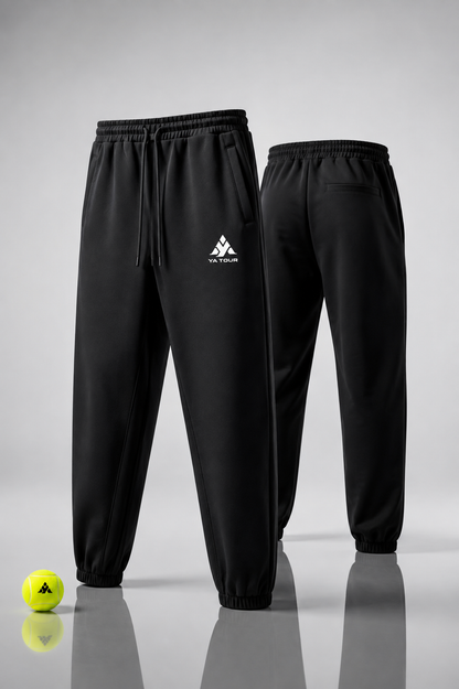 YA TOUR Unisex Heavyweight Fleece Joggers – Black, front and back editorial view showing mid-rise elastic waistband with drawstring, YA TOUR logo, side pockets and tapered ankle cuff, styled with a YA TOUR tennis ball